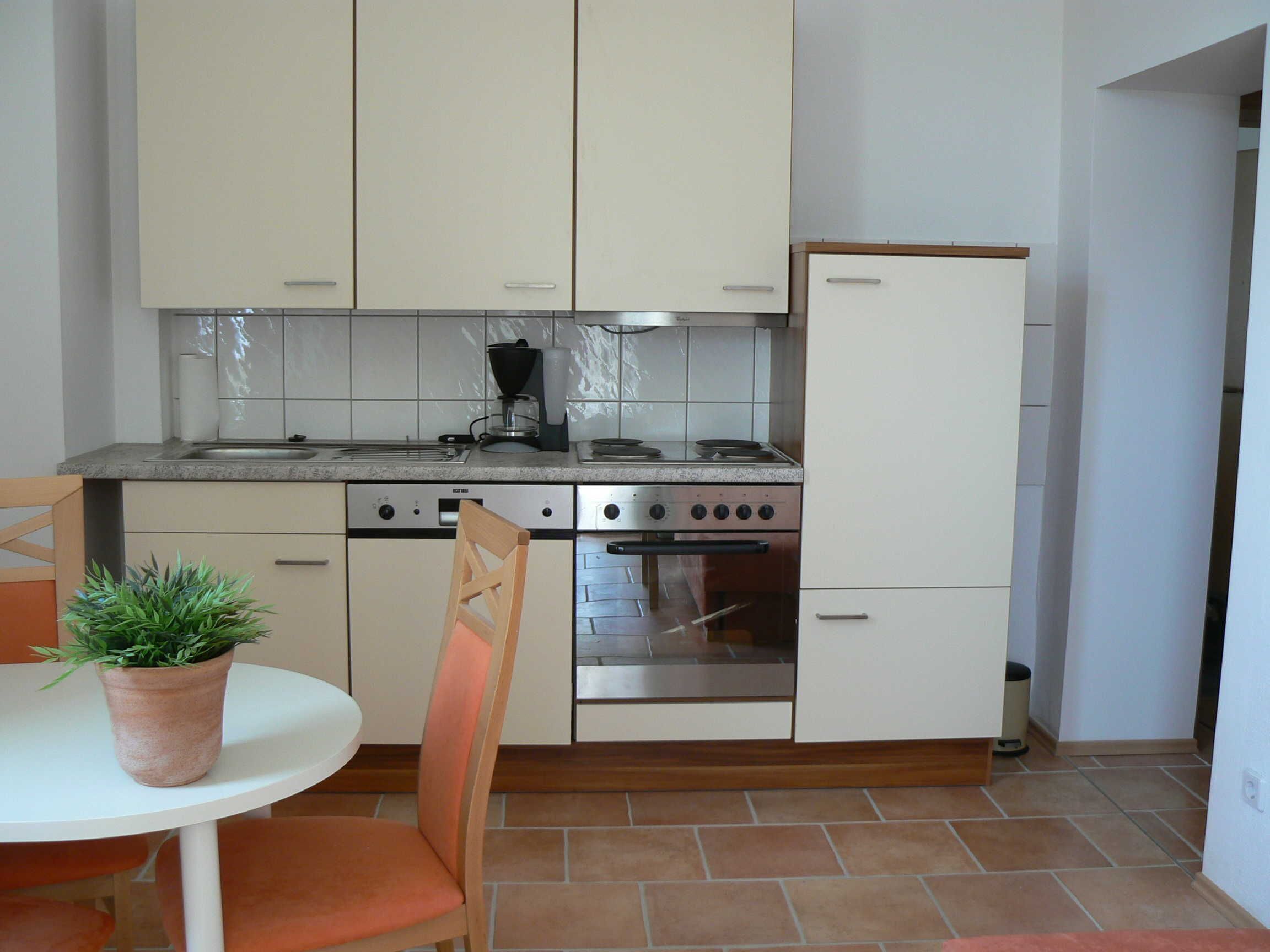 Een kleine keuken met witte kastjes, een fornuis, oven en een koelkast.