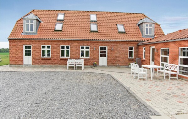 A red brick building with multiple windows, a gravel driveway, and outdoor seating.