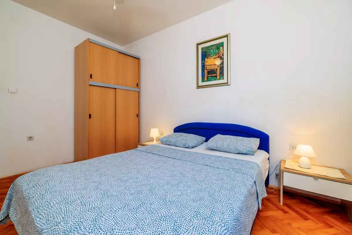 A bedroom with a bed, two bedside tables with lamps, a wardrobe, and a framed picture on the wall.