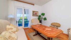A room with a wooden dining table, a sofa with patterned cushions, a chair, a potted plant, and a view through a glass door. - Holiday apartment with grill and wifi (Jadranovo)