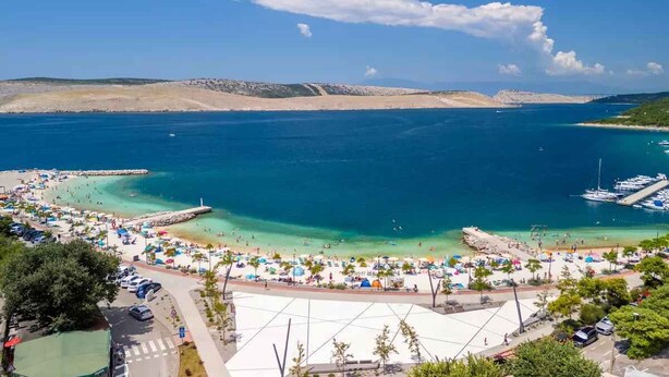 A coastal beach area with clear blue waters, a sandy beach, and a marina with boats. - Holiday apartment with grill and wifi (Jadranovo)