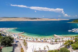A coastal beach area with clear blue waters, a sandy beach, and a marina with boats. - Holiday apartment with grill and wifi (Jadranovo)