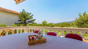 A round table with a tray of items, red chairs, and a view of greenery and a building in the background. - Holiday apartment with grill and wifi (Jadranovo)