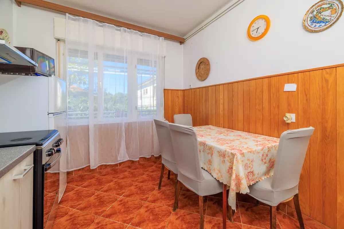 Eine kleine Küche mit Herd, einem Esstisch mit Stühlen und einem Fenster mit durchsichtigen Vorhängen.