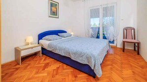 A bedroom with a bed, a nightstand, a chair, and a window with curtains. - Holiday apartment with grill and wifi (Jadranovo)