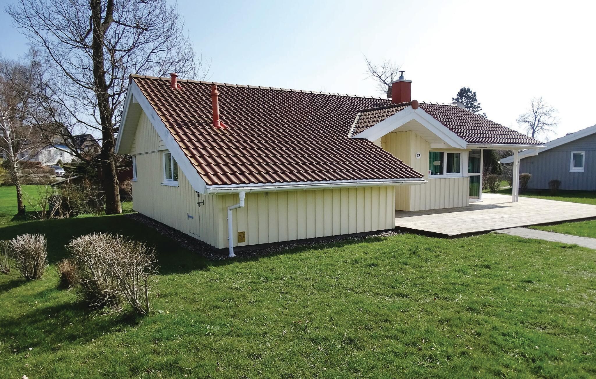 Een gelijkvloers huis met een schuin dak, schoorsteen en een klein terras.