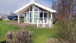Une petite maison à un étage, dotée d’un toit en pente, de grandes fenêtres et d’une terrasse entourée d’une clôture.