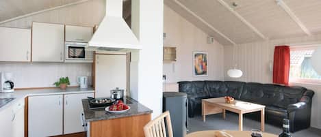 A compact kitchen with a microwave, coffee maker, and a dining area with a table set for two, a sofa, and a red curtain.