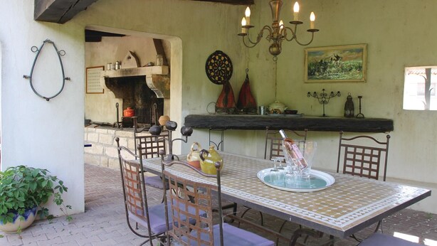 A rustic dining area with a tiled table, metal chairs, a chandelier, a dartboard, and a fireplace. - 2 bedroom beautiful home in Bellegarde (Bellegarde)