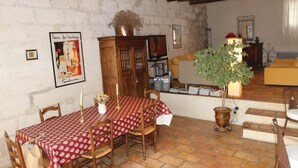 A dining area with a red patterned tablecloth, wooden chairs, a potted plant, and a rustic stone wall. - 2 bedroom beautiful home in Bellegarde (Bellegarde)