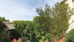 A courtyard with a tree, a red chair, and a stone wall. - 2 bedroom beautiful home in Bellegarde (Bellegarde)
