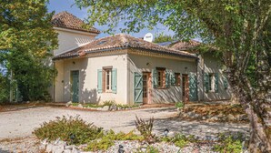 A two-story house with a tiled roof, green shutters, and a gravel driveway.