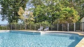 A swimming pool with clear water, surrounded by a fence and trees. There are two lounge chairs by the pool.