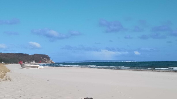 Une plage avec un rivage sablonneux, une falaise rocheuse en arrière-plan et un ciel dégagé.
