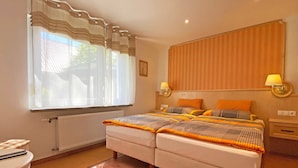 Un lit double avec une couvre-lit à rayures, deux tables de chevet avec des lampes, une fenêtre avec des rideaux légers et un radiateur.