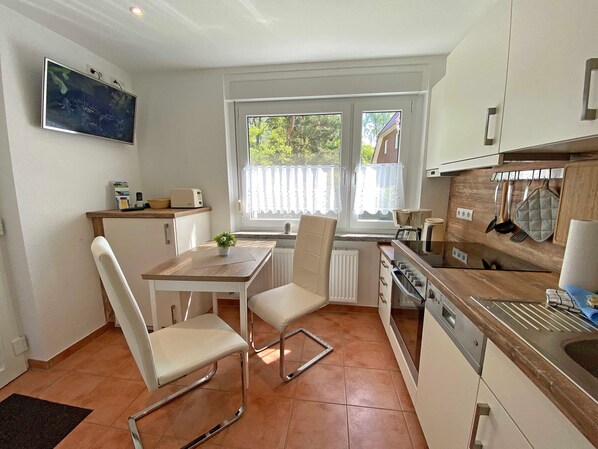 Una cocina compacta con una mesa, sillas, una pequeña planta en maceta y una ventana con cortinas.