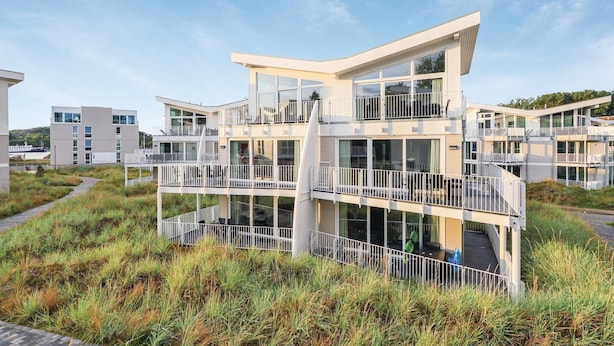 A modern multi-story building with balconies and large windows, surrounded by grassy terrain. - 3 bedroom beautiful apartment in Travemünde Waterfront (Travemünde Waterfront)