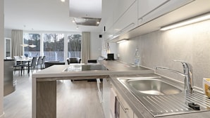 A modern kitchen with a central island, stainless steel appliances, and a view of the outdoors through large windows. - 3 bedroom beautiful apartment in Travemünde Waterfront (Travemünde Waterfront)