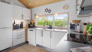 A modern kitchen with white cabinets, a built-in oven, and a window with a view of greenery. - Cozy home in Nakskov with kitchen (Nakskov)