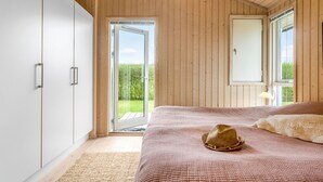 A bedroom with a large bed, wooden walls, a sliding glass door leading to a garden, and a ceiling light fixture. - Cozy home in Nakskov with kitchen (Nakskov)