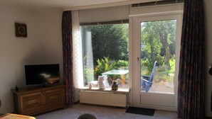Ein Wohnzimmer mit Fernseher, einer Couch, einem Couchtisch und einer Glastür zum Garten.