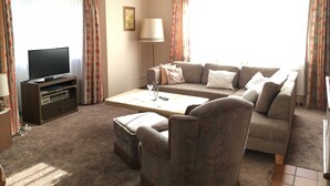 Ein Wohnzimmer mit Flachbildfernseher, einer Couch, einem Couchtisch und einem Sessel.