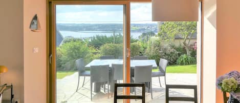 Une pièce dotée d’une porte-fenêtre coulissante donnant sur une terrasse extérieure avec une table et des chaises, un vase rempli de fleurs et une lampe.