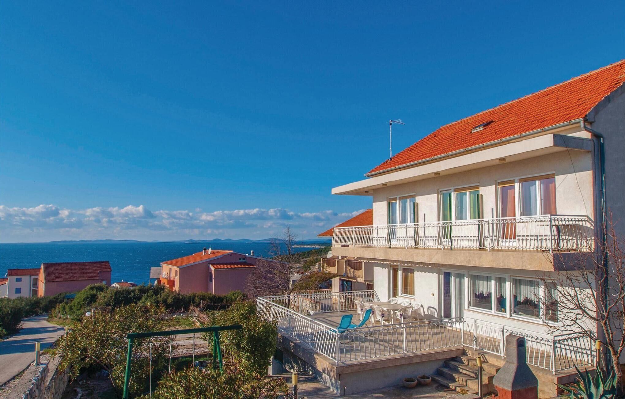 Ein zweistöckiges Gebäude mit einem Balkon und Blick auf das Meer, unter einem wolkenlosen Himmel.