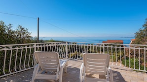 Twee witte plastic stoelen op een balkon met een metalen hek, met uitzicht op een heldere blauwe zee en land in de verte.
