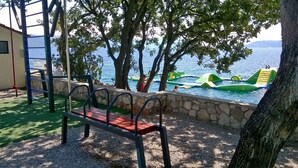 A playground with a bench, a climbing structure, and inflatable water toys by a body of water. - Holiday apartment with 24 square meter terrace (Novi Vinodolski)