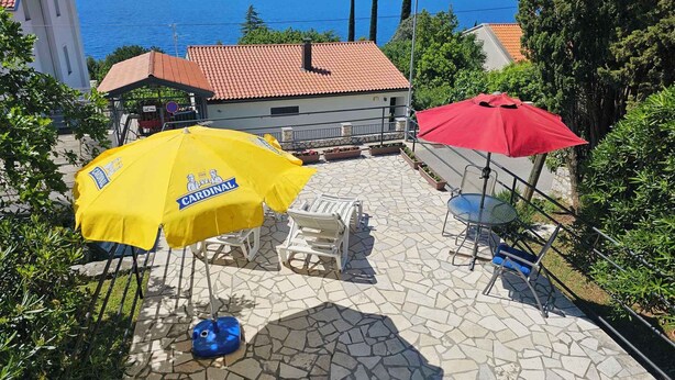A patio with outdoor seating, a yellow and a red umbrella, and a view of the sea. - Holiday apartment with 24 square meter terrace (Novi Vinodolski)