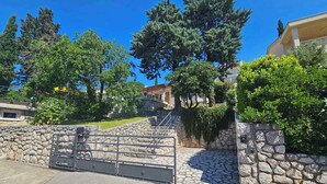 A gated entrance with stone walls and a metal gate, surrounded by greenery and trees. - Holiday apartment with 24 square meter terrace (Novi Vinodolski)