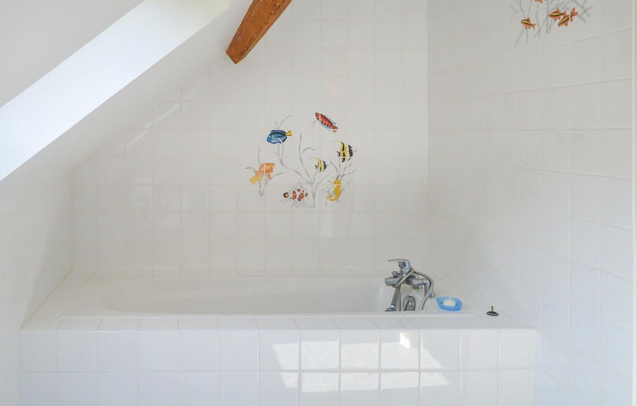 A bathroom with a white tiled wall, a bathtub, and a wooden ceiling beam.