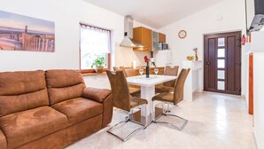 Una sala moderna con un sofá de cuero marrón, una mesa de comedor con cuatro sillas y una zona de cocina con armarios de madera y un microondas.