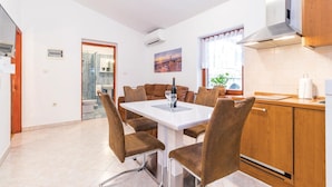 Cocina moderna con comedor, que incluye una mesa blanca, sillas marrones y una campana extractora de acero inoxidable.