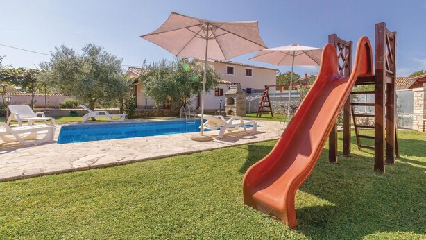 Un patio trasero con piscina, tobogán y sillas de descanso.