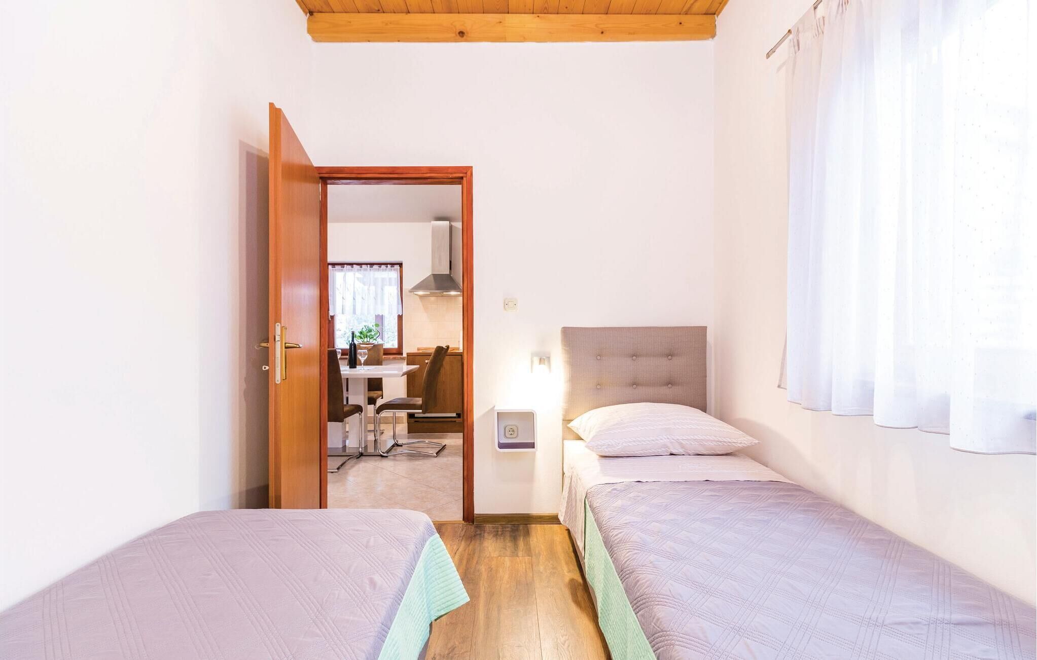 Una stanza con due letti singoli, soffitto in legno, una porta che dà su un'area pranzo e una finestra con tende.