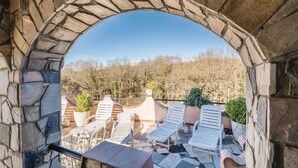 Un arco de piedra que da paso a un patio con sillones blancos y plantas en macetas.