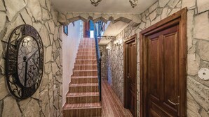 Un pasillo con paredes de piedra, una puerta de madera y una escalera que sube a un nivel superior.