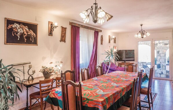 Un comedor con una mesa larga, sillas, una araña y un televisor.