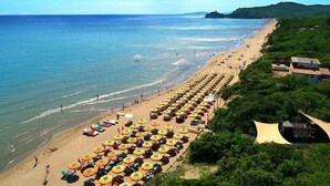 A beach with rows of sunbeds and umbrellas, a clear view of the sea, and a building on the right. - Bungalow in the Rocchette Holiday Resort (Castiglione della Pescaia)