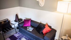 A modern living room with a grey sofa, black and red cushions, a magazine, a lamp, and a wall-mounted deer head decoration. - Bungalow in the Rocchette Holiday Resort (Castiglione della Pescaia)