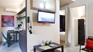 A modern living room with a flat-screen TV, a dining area with a table and chairs, and a kitchen area with a counter and cabinets. - Bungalow in the Rocchette Holiday Resort (Castiglione della Pescaia)