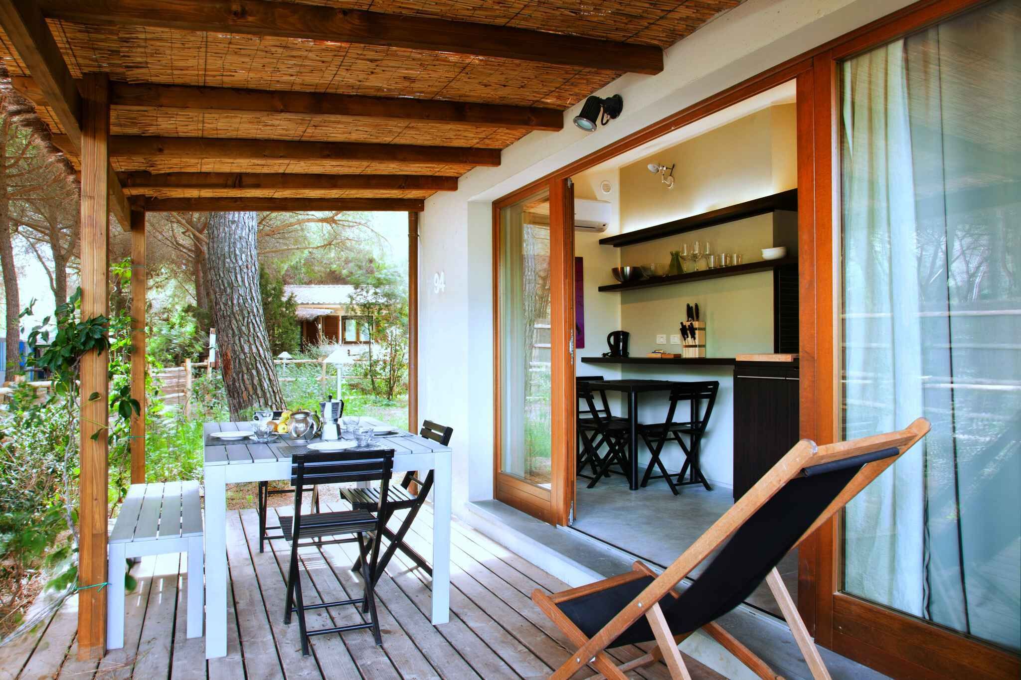 An outdoor wooden deck with a table and chairs, a wooden bench, and a glass door leading to a kitchen area.