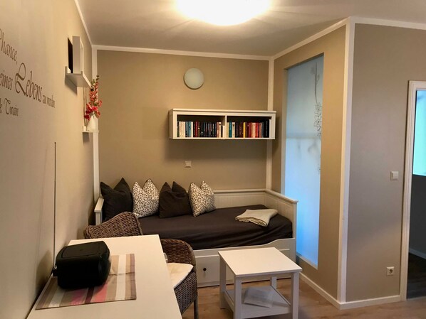 Un salon confortable avec un canapé, une petite table, une bibliothèque et une horloge fixée au mur.