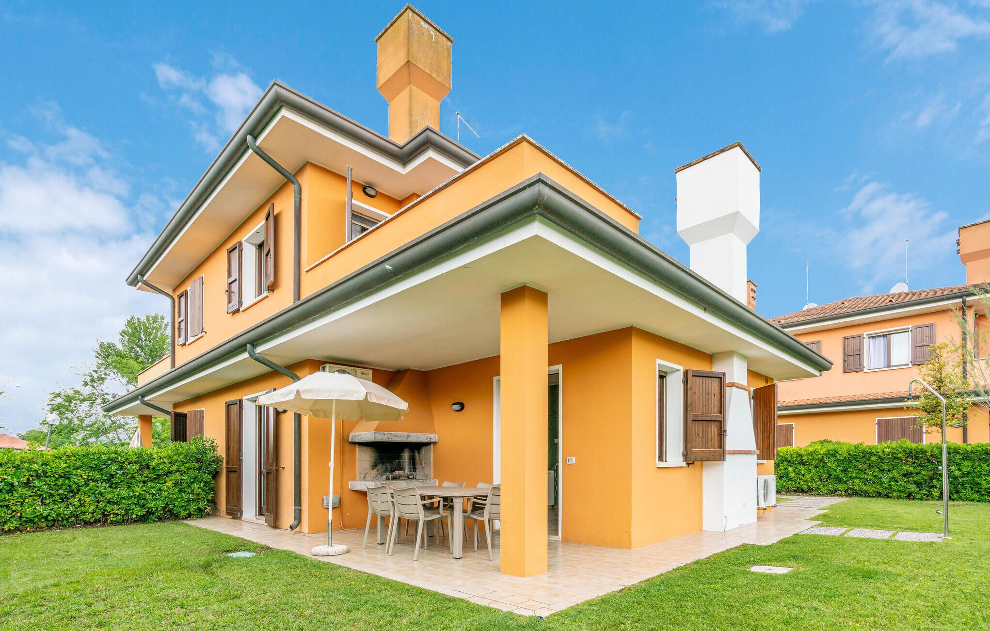 Una casa de dos pisos con un porche cubierto, mobiliario exterior y una chimenea.