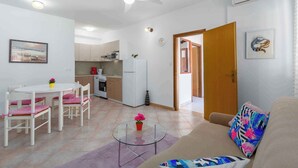 Een moderne woonkamer met een glazen salontafel, een beige bank en een eethoek met witte stoelen.