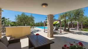 Een terras buiten met een zwembad, zitplaatsen en een pergola met parasols.