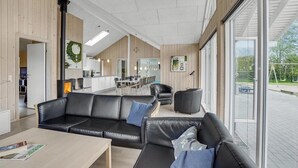 Un interior moderno con un sofá de cuero negro, una mesa de comedor de madera y ventanas amplias que ofrecen vistas al exterior.