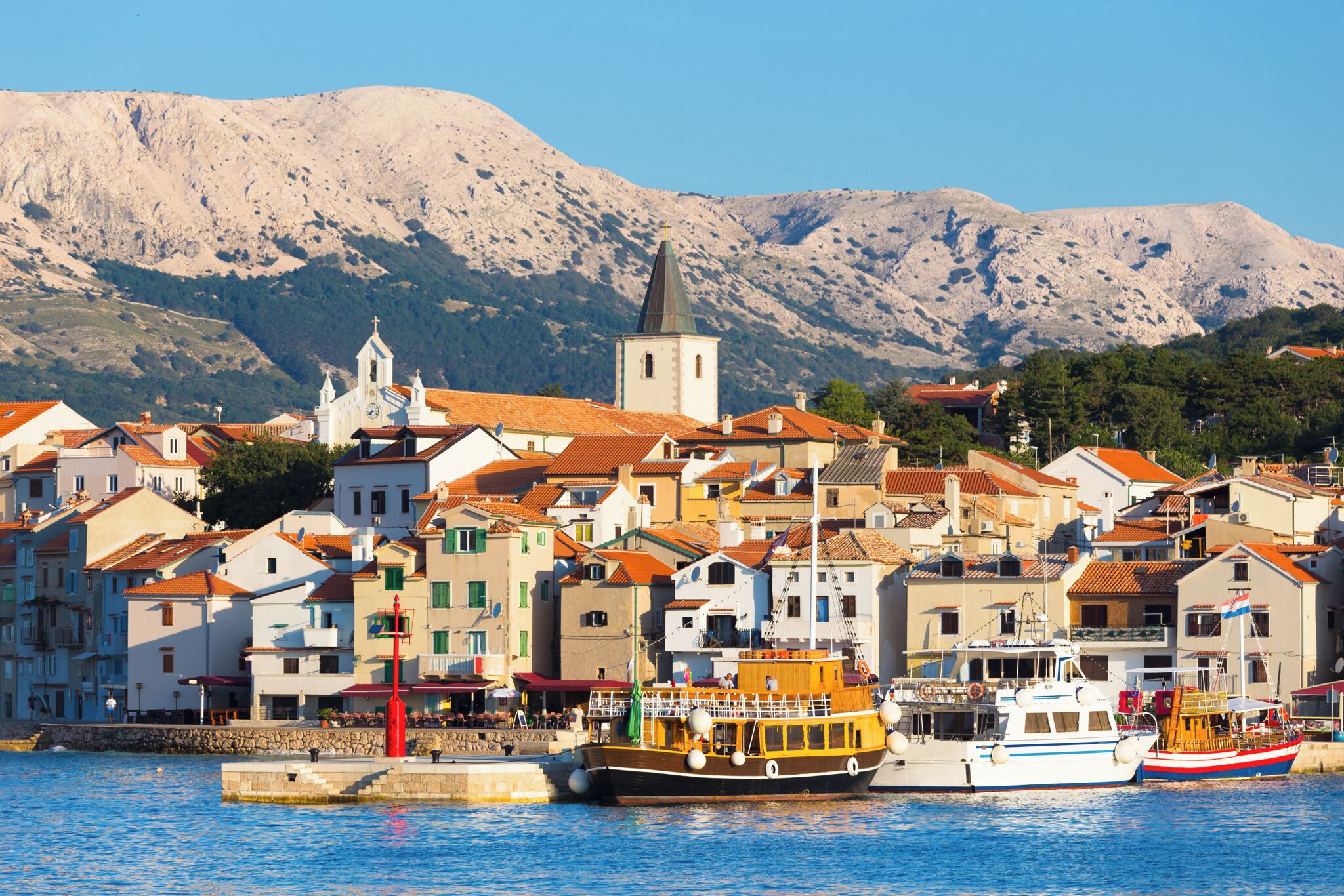 Une ville côtière dotée de bâtiments historiques, d’une église et de bateaux amarrés dans le port.
